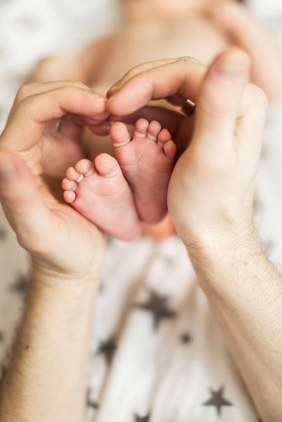 Ο μπαμπάς κρατάει στα χέρια του τα πόδια του παιδιού του. Η έννοια της ευτυχισμένης οικογένειας. αρσενικά χέρια πατεράδες και πόδια babys - Φωτογραφία, εικόνα