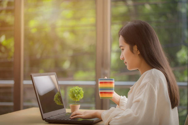 Женщина, работающая с ноутбуком, сидя дома в офисе, пьет кофе, предупреждает о социальной отдаленности, остается дома, чтобы избежать вирусной инфекции, коронавируса или COVID-19 вспышки
 - Фото, изображение