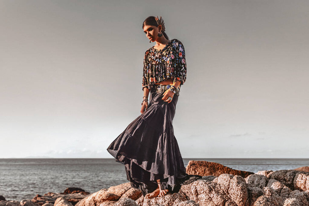 beautiful young fashionable woman on the rocks at sunset - Foto, Imagen