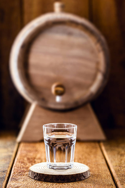 Old oak barrel and glass of high quality distilled alcohol. Brazilian silver cachaca, called pinga, vodka, white rum, liqueur, pure drink, Poitn, sake, brandy or Absinthe. - Photo, Image