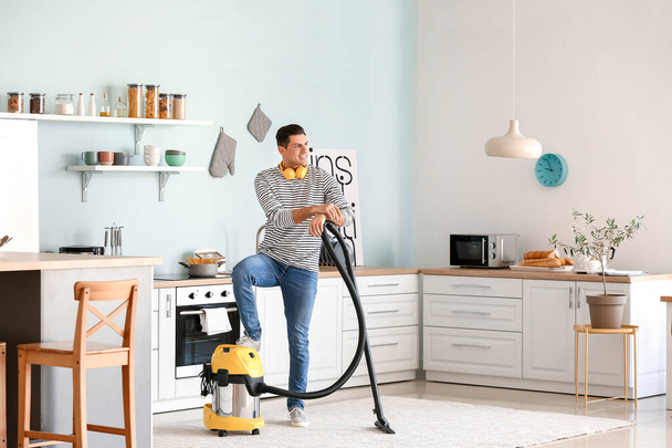 Young man hoovering floor in kitchen - Photo, Image