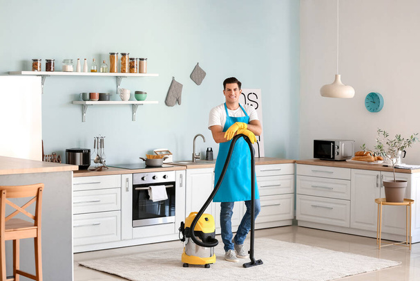 Young man with vacuum cleaner in kitchen - 写真・画像