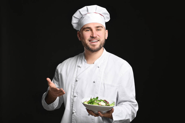 Bonito chef masculino com salada no fundo escuro
 - Foto, Imagem