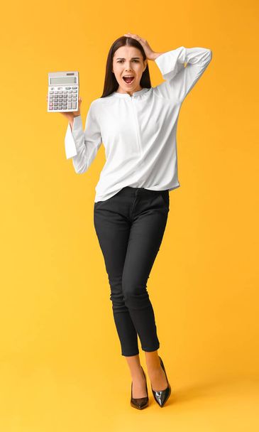 vervloekte jonge vrouw met rekenmachine op kleur achtergrond - Foto, afbeelding