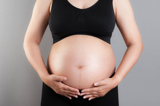 Großaufnahme Bauch einer schwangeren Frau vor grauem Hintergrund - Foto, Bild