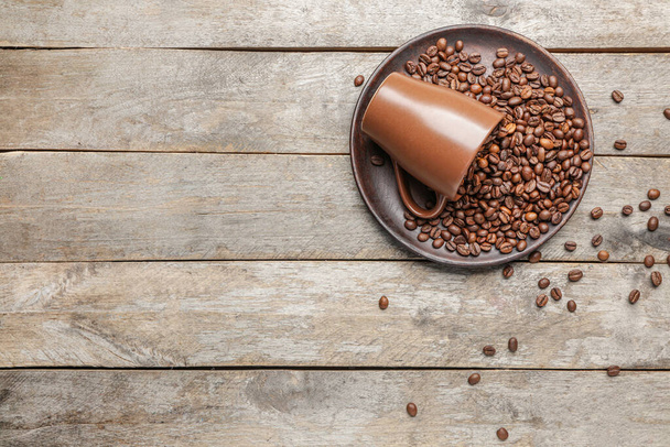 Cup and plate with coffee beans on wooden background - Foto, Imagen