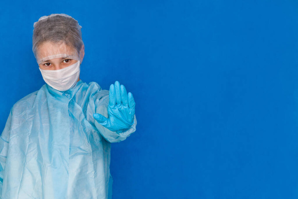 Giovane operatore medico su sfondo blu in guanti e maschera che tiene la mano simboleggia stop
. - Foto, immagini