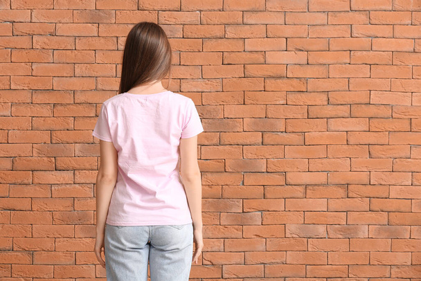 Mladá žena ve stylovém tričku na cihlovém pozadí - Fotografie, Obrázek