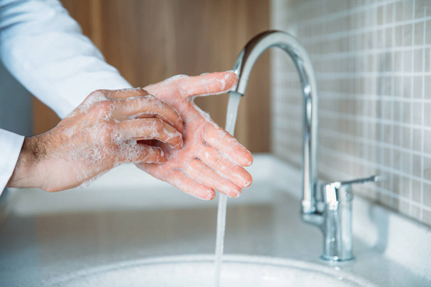 Ο άνθρωπος πλένει σωστά τα χέρια με σαπούνι για να προστατεύεται από τον ιό Coronavirus 2019-nCoV πανδημική επιδημία λοίμωξης. Ο γιατρός δείχνει πώς να πλένει σωστά τα χέρια. - Φωτογραφία, εικόνα