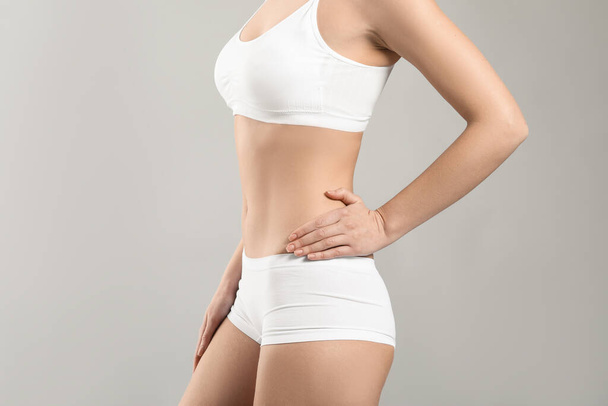 Молодая женщина в нижнем белье на сером фоне. Концепция пластической хирургии - Фото, изображение