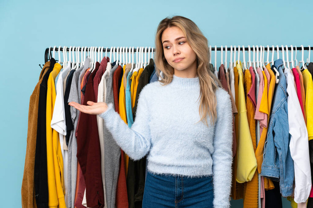 Teenager Russian girl buying some clothes isolated on blue background holding copyspace with doubts - 写真・画像