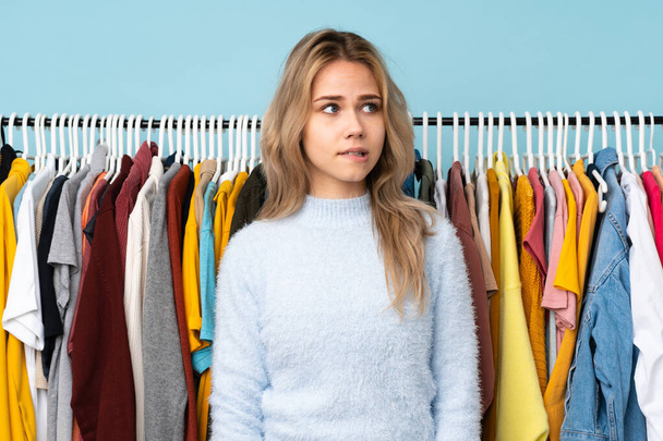 Teenager Russian girl buying some clothes isolated on blue background with confuse face expression - Fotoğraf, Görsel