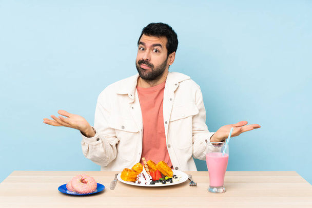 Человек за столом, завтракающий вафлями и молочный коктейль, сомневающийся, поднимая руки
 - Фото, изображение