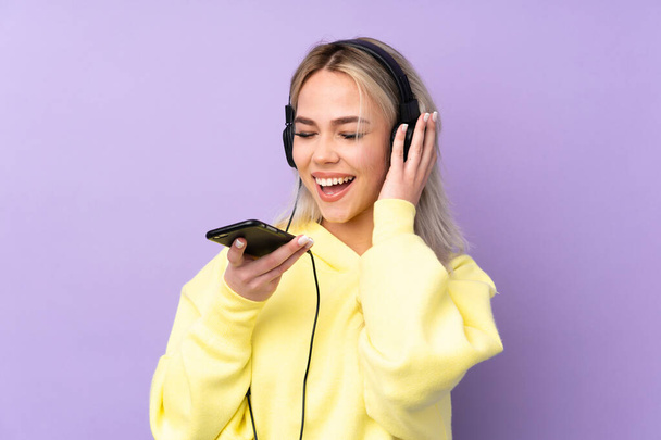 Teenager lány felett elszigetelt lila háttér zenét hallgat egy mobil és énekel - Fotó, kép
