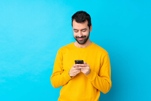 Fiatal fehér férfi izolált kék háttér küld egy üzenetet a mobil - Fotó, kép