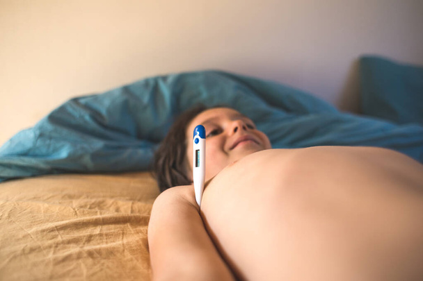 Un garçon avec de la fièvre est couché, Un enfant mesure la température corporelle avec un thermomètre
. - Photo, image