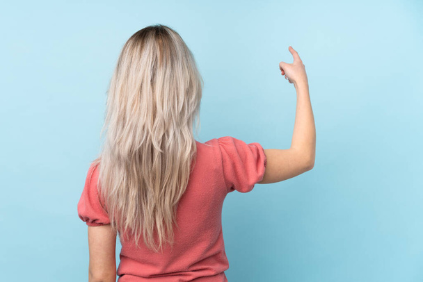 Chica adolescente sobre fondo azul aislado apuntando hacia atrás con el dedo índice
 - Foto, Imagen