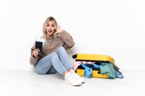 Подростковая блондинка с чемоданом, полным одежды, сидящей на полу, делает телефонный жест. Перезвони мне
 - Фото, изображение