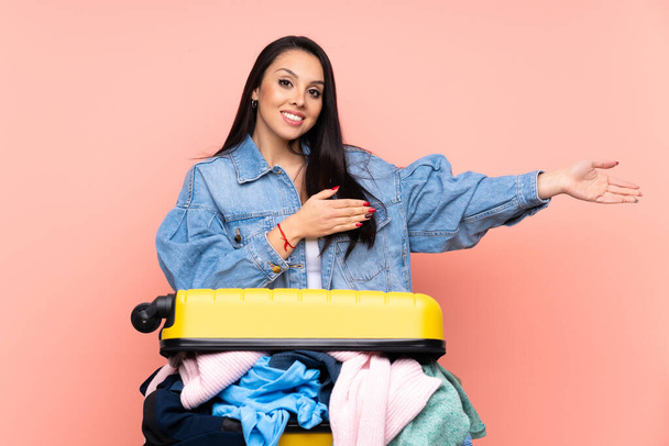 Traveler Colombian girl with a suitcase full of clothes over isolated pink background extending hands to the side for inviting to come - Photo, Image