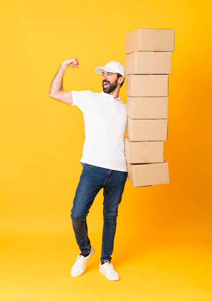 Full-length shot of delivery man among boxes over isolated yellow background - Valokuva, kuva