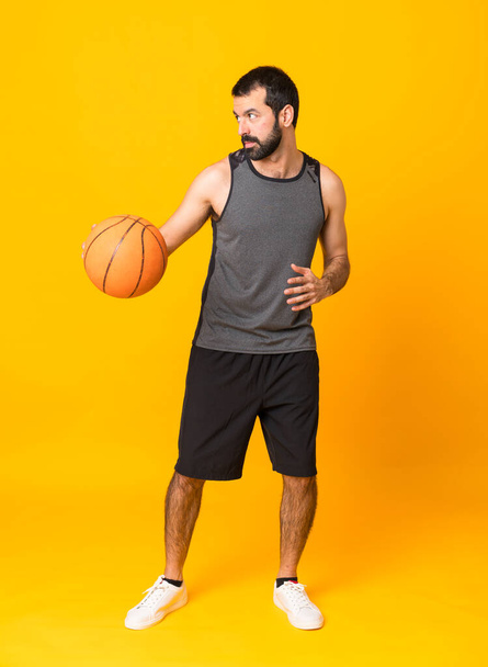 Full-length shot van een man die basketbal speelt over geïsoleerde gele achtergrond - Foto, afbeelding