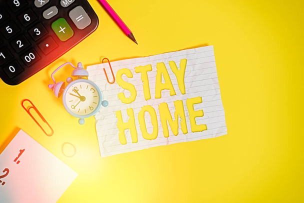 「 Stay Home 」を示すテキスト記号。コンセプト写真は活動のために外出し、家や家の中に滞在しない目覚まし時計クリップノートゴムバンド電卓鉛筆色の背景. - 写真・画像
