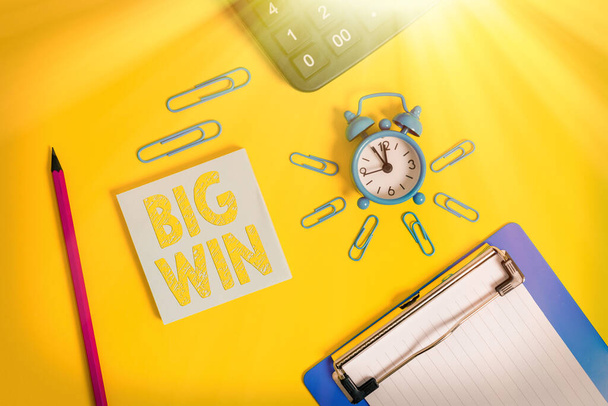 Writing note showing Big Win. Business photo showcasing having won an important prize Money won by success in a game Alarm clock clipboard pencil calculator notepad colored background. - Photo, Image