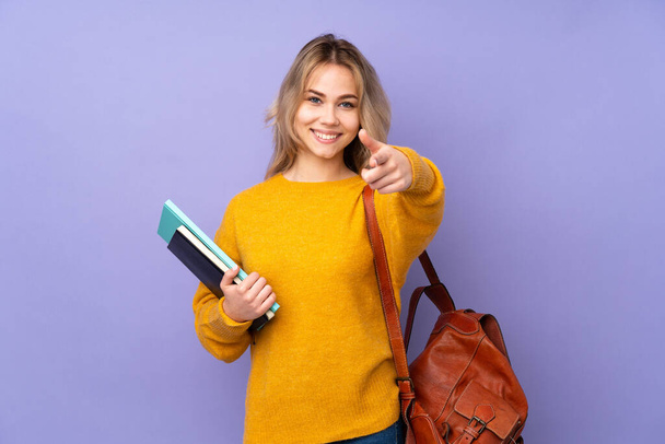 Teenager rusky student dívka izolované na fialovém pozadí ukazuje na přední a usmívá - Fotografie, Obrázek