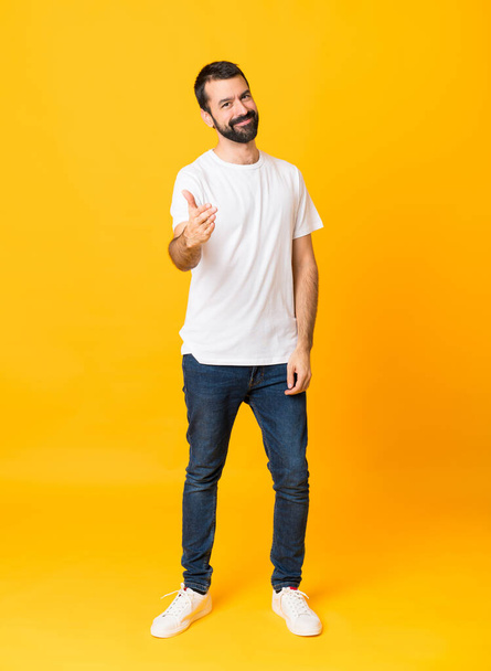 Full-length shot of man with beard over isolated yellow background shaking hands for closing a good deal - 写真・画像