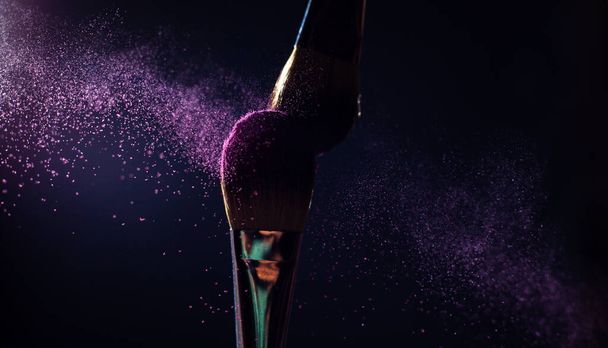 Art of visage.  Closeup photo of two professional black make-up brushes with purple  powder isolated on black background with copy place.  - Photo, image