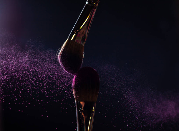 Art of visage.  Closeup photo of two professional black make-up brushes with purple  powder isolated on black background with copy place.  - 写真・画像