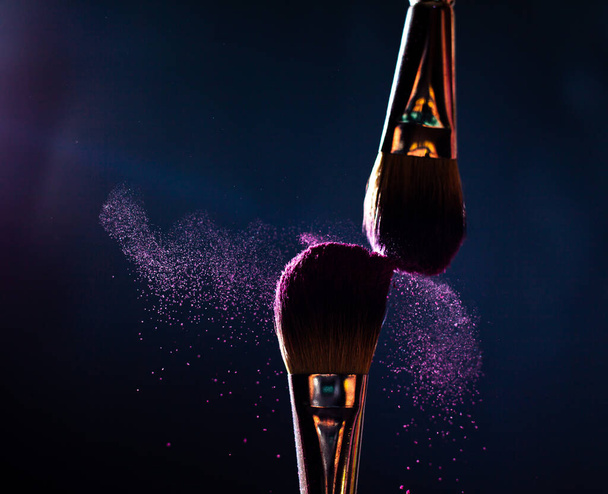 Arte del rostro. Foto de cerca de dos pinceles profesionales de maquillaje negro con polvo púrpura aislado sobre fondo negro con lugar de copia
.  - Foto, imagen