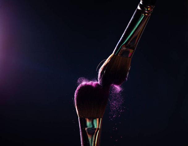 Art of visage.  Closeup photo of two professional black make-up brushes with purple  powder isolated on black background with copy place.  - Foto, Imagem