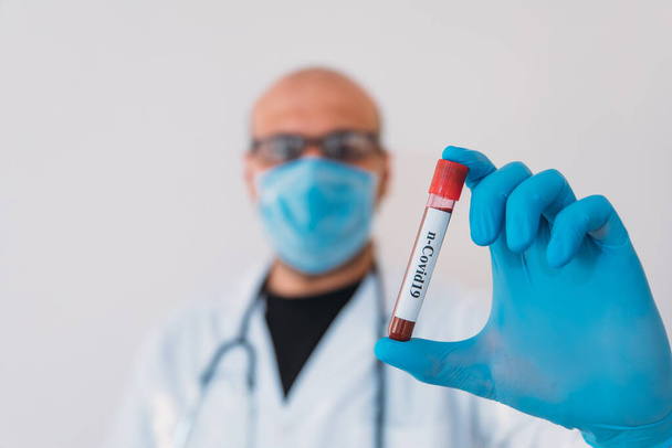 Doctor Holding Pandemic Coronavirus 2019-nCoV Blood Sample Positive Test Tube. Lékař nosí lékařskou masku a rukavice a ukazuje pacientovi krevní zkumavku obsahující virus korony (COVID-19) - Fotografie, Obrázek
