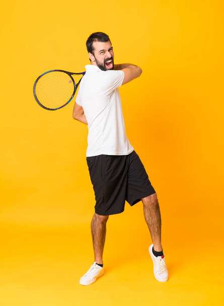 Full-length shot of man playing tennis over isolated yellow background - Photo, Image