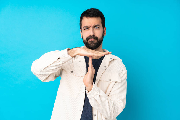 Young handsome man with white corduroy jacket over isolated blue background making time out gesture - Foto, Imagem