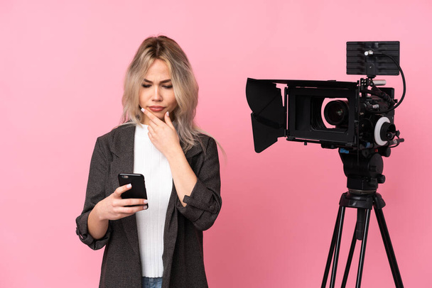 Reportera mujer sosteniendo un micrófono y reportando noticias sobre el fondo rosa aislado pensando y enviando un mensaje
 - Foto, imagen