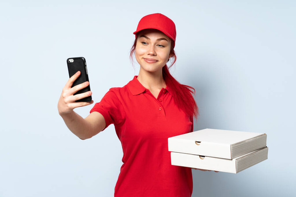 Repartidor de pizza sosteniendo una pizza sobre un fondo aislado haciendo una selfie
 - Foto, imagen