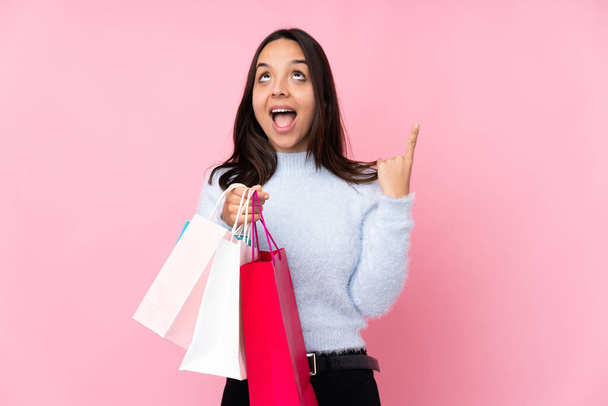 Mujer joven con bolsa de compras sobre fondo rosa aislado apuntando hacia arriba y sorprendido
 - Foto, Imagen