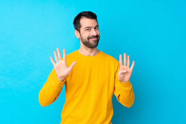 Jonge blanke man over geïsoleerde blauwe achtergrond tellen negen met vingers - Foto, afbeelding
