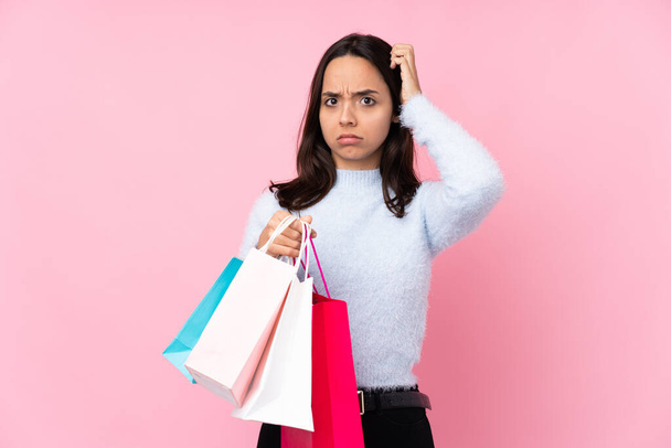 Mladá žena s nákupní taškou přes izolované růžové pozadí s pochybnostmi - Fotografie, Obrázek
