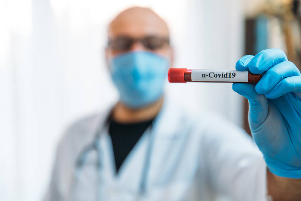 Doctor Holding Pandemic Coronavirus 2019-nCoV Αίμα δείγμα θετική σωλήνα δοκιμής. Γιατρός που φοράει ιατρική μάσκα και γάντια και δείχνει το σωλήνα εξέτασης αίματος του ασθενούς που περιέχει τον ιό του στέμματος (COVID-19)) - Φωτογραφία, εικόνα