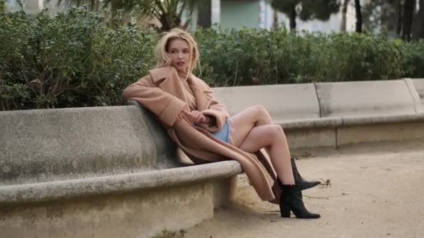 Romantisch stijlvol blond meisje dromerig rusten op bank in stadspark - Video