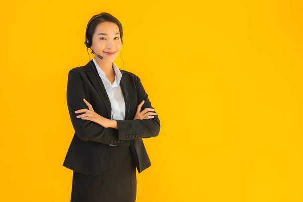 Портрет красивая молодая деловая азиатка с наушниками или наушниками для колл-центра или телемаркетинга на желтом изолированном фоне
 - Фото, изображение