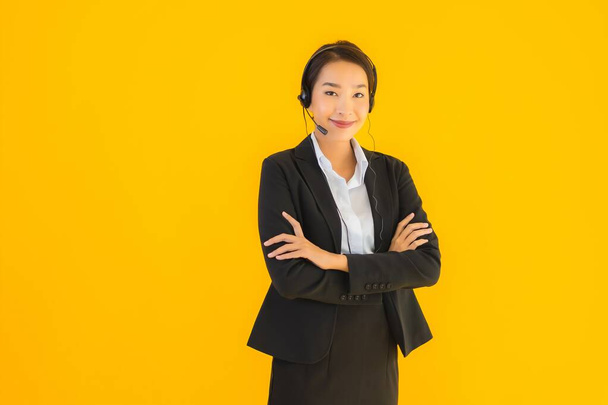 Porträt schöne junge asiatische Geschäftsfrau mit Kopfhörer oder Headset für Call Center oder Telemarketing auf gelbem Hintergrund - Foto, Bild