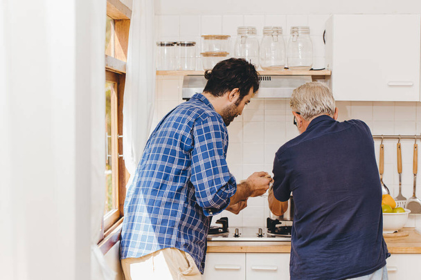Oudere koken in de keuken met familie jongeman voor een verblijf thuis activiteit samen. - Foto, afbeelding