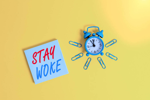 Conceptual hand writing showing Stay Woke. Business photo showcasing being aware of your surroundings and things going on Keep informed Metal vintage alarm clock clips notepad colored background. - Photo, Image