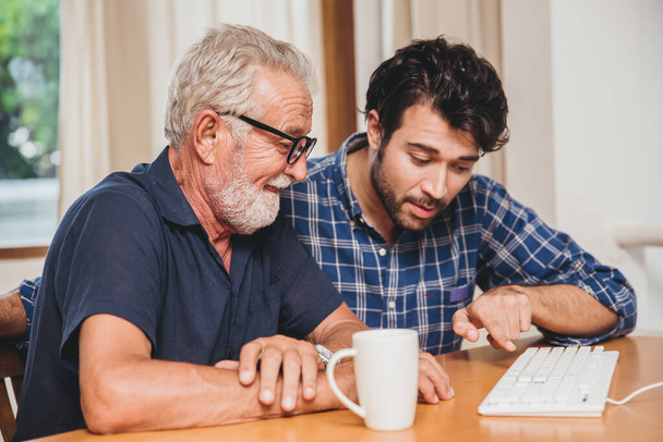 jonge man of zoon leren zijn opa de oudere vader leren om computer te gebruiken thuis. - Foto, afbeelding