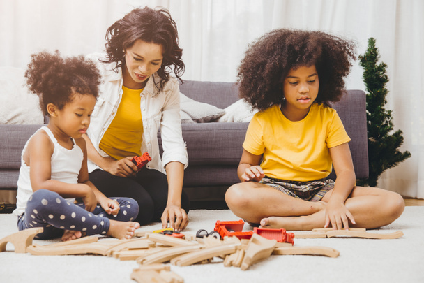 シングルマザーは2人の娘と一緒に家のアパートでパズルのおもちゃを学び、遊んでいます。リビングルームで誰もが探しているか育児黒の人々. - 写真・画像