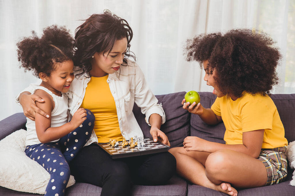 Samotna mama dobra opieka, ucząc swoje dzieci być genialne i sprytne małe dziewczynki uczy się grać w szachy gra planszowa jedzenie owoców dla zdrowych. - Zdjęcie, obraz